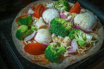 healthy cheat day homemade pizza with broccoli tomato red onion parmesan and tomato sauce before insert in the oven 