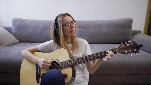 Woman in headphones plays the guitar at her home, happily having fun playing guitar and singing
