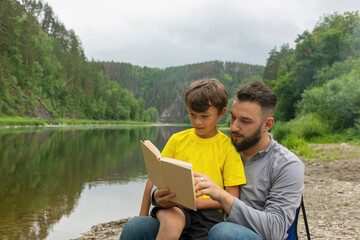 man and boy reading book on vacation, spending time on nature