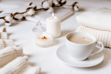 Obraz na płótnie Canvas Details of still life in the home interior of living room. Cup of coffee, cotton, book, candle, sweater. Moody. Cosy autumn winter concept on white background. Decoration.