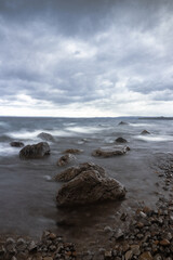 piedras en orilla de playa con agua sedosa en día nublado