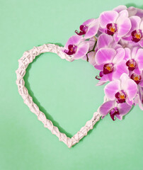 Beautiful pink orchid bloom laying next to rustic white heart on pastel green background.
