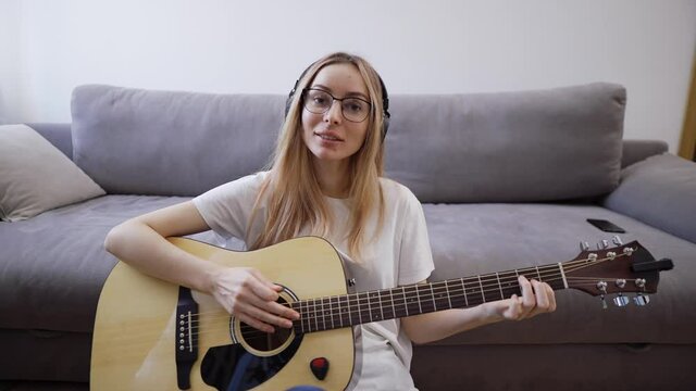 Woman plays the guitar at her home, happily having fun playing guitar and singing