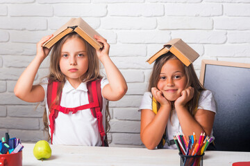 School girls. Friendship of small sisters in classroom at knowledge day. Back to school and home schooling. sad school kids at lesson. Little girls with books on head.