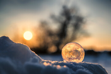 Romantische Aufnahme einer im Schnee liegenden gefrorenen Seifenblase im Sonnenuntergang