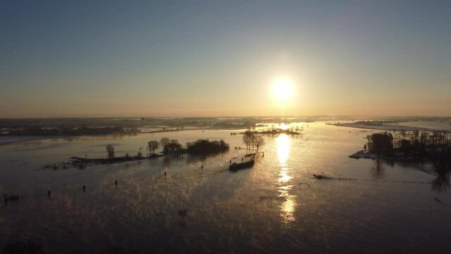 Ship sailing in a foggy winter sunrise over the river Ijssel with ice and snow during a cold day in The Netherlands. Aerial drone point of view.