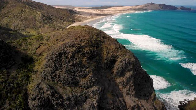 Man Standing On Hill Admiring Ocean Waves Rolling On Sandy Shore Of Te Werahi Beach, National Park In Northland, New Zealand. - aerial