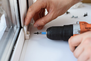 Man installing gray pleated blinds on the window with screwdriver