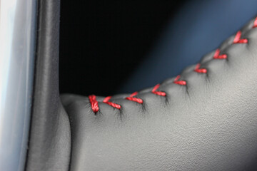 Red stitches on a black leather steering wheel