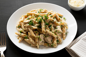 Homemade Chicken Alfredo Penne with Parsley on a black surface, side view.