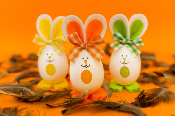 Three Easter eggs with bunny ears on spring yellow background.