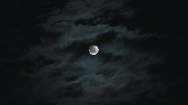 Dark clouds passing in front of a bright full moon during the night