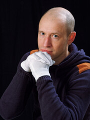 portrait of a bald man in white gloves on a black background