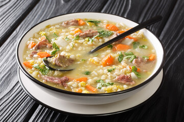 Scotch broth is a Scottish soup traditionally featuring barley, a meat lamb, root vegetables  closeup in the plate on the table. Horizontal