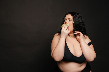 Plus size model in lingerie, fat sexy woman in underwear on black studio background, body positive concept, full length portrait,a beautiful plus size model holds an apple in her hand