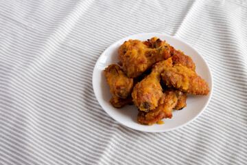 Homemade Spicy Mango Chicken Wings on a white plate on cloth, side view. Copy space.