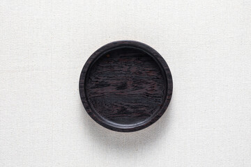 Dark black handmade round wooden plate on burlap. Round tray. 