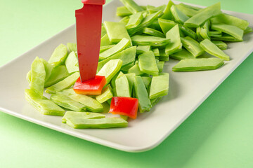 Green beans and chunks of pepper on a plate with a red knife