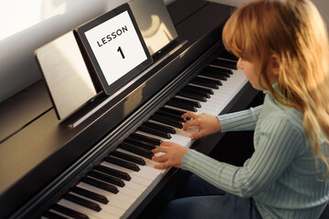 A little girl learns to play the piano from video lessons. Online distance learning during covid-19. New normal