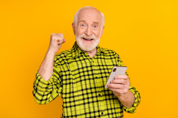 Photo of crazy mature man hold telephone raise fist rejoice wear plaid green shirt isolated yellow...