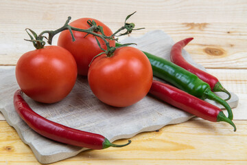 3 Tomaten und 4 Peperoni auf einem Holzbrett.