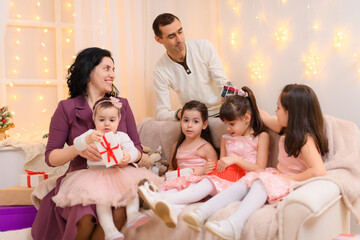 family portrait of a parents and children, sitting on a couch in home interior decorated with lights and gifts