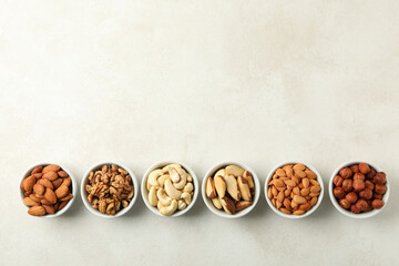 Bowls with different nuts on white textured background, space for text