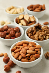 Bowls with different nuts on white textured background, space for text