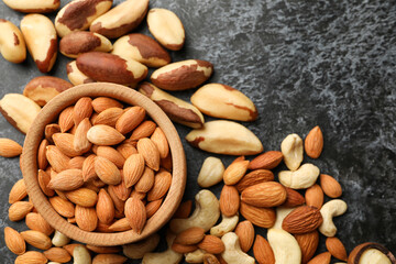 Wooden bowl with almonds and different nuts on black smokey background, space for text