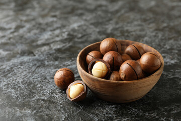 Bowl with tasty macadamia nuts on black smokey background