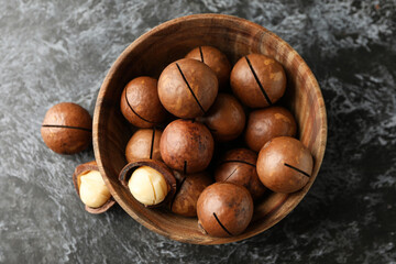 Bowl with tasty macadamia nuts on black smokey background