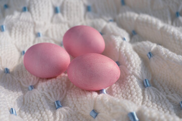 Fototapeta na wymiar Three pink Easter eggs on a white knitted blanket