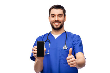 medicine, healthcare and technology concept - happy smiling doctor or male nurse in blue uniform with smartphone and stethoscope showing thumbs up over white background