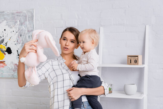 Young Mother Holding Baby Boy And Toy Bunny At Home