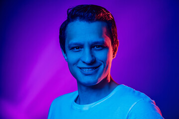 Caucasian man's portrait on purple blue studio background in multicolored neon light. Beautiful male model. Concept of human emotions, facial expression, sales, ad, fashion. Copyspace.