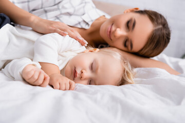 Fototapeta na wymiar surface level of happy woman with closed eyes touching sleeping son, blurred background