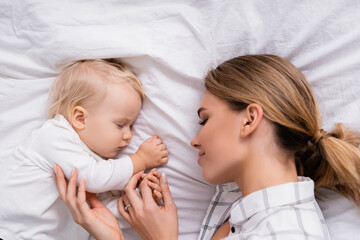 top view of happy woman touching hand of little son sleeping on white bedding