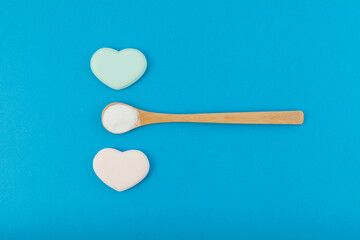 White powder in wooden spoon on blue background with hearts. Top view, copy space