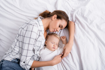 top view of young mother sleeping with toddler son on white bedding
