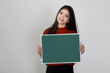 Happy young pretty female smiling at camera holding blank chalkboard,  showing something interesting and exciting on slate with copy space for text.