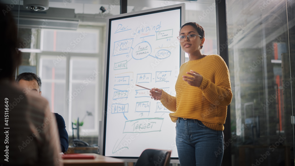 Poster Project Manager Makes a Presentation for a Young Diverse Creative Team in Meeting Room in an Agency. Colleagues Sit Behind Conference Table and Discuss Business Development, User Interface and Design.