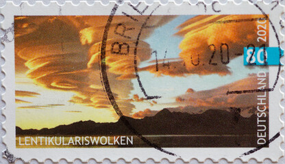 GERMANY - CIRCA 2020: a postage stamp printed in Germany showing a mountain silhouette and cloudscape Text: Lenticularis clouds