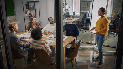 Project Manager Makes a Presentation for a Young Diverse Creative Team in Meeting Room in an...