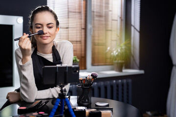 Beautiful girl does makeup on the camera. On the table are makeup brushes and palettes. Online learning concept. Blogging.