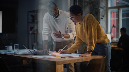 Two Diverse Multiethnic Colleagues Have a Conversation in a Meeting Room Behind Glass Walls in an Agency. African American Creative Director and Female Project Manager Discuss Work on Laptop Computer.