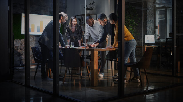 Young Creative Team Meeting with Business Partners in Conference Room Behind Glass Walls in Agency. Colleagues Sit Behind Conference Table and Discuss Business Opportunities, Growth and Development.