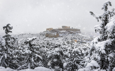 View through snow covered trees to the Parthenon Temple and Herodion Theatre at the Acropolis of Athens, Grece, with heavy snowfall during winter
