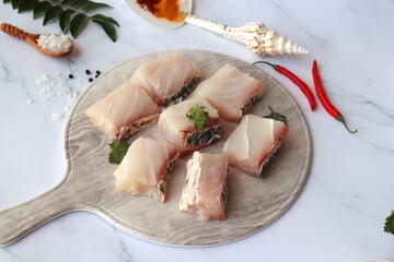 Uncooked boneless pieces of threadfin fish. Raw Dadha fish cubes placed on a blue plate. clean fish fillets with skin on. Recipe ingredients such as rock salt, coriander, and spices. Copy space.