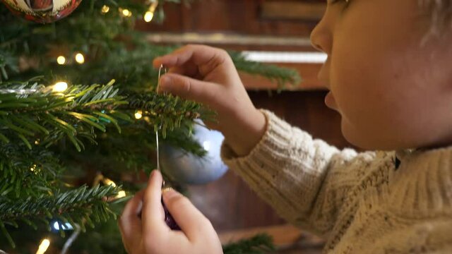 Cute Little Boy Decorates Christmas Tree with Toys. Close-up Child Face Hands. x2 Slow motion 60fps 4K