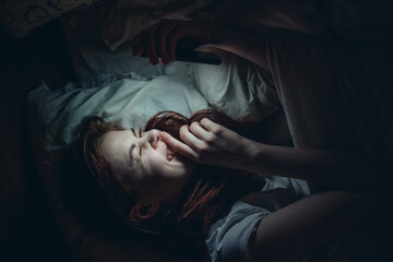 emotional woman with a phone in her hands lies in bed at night addiction